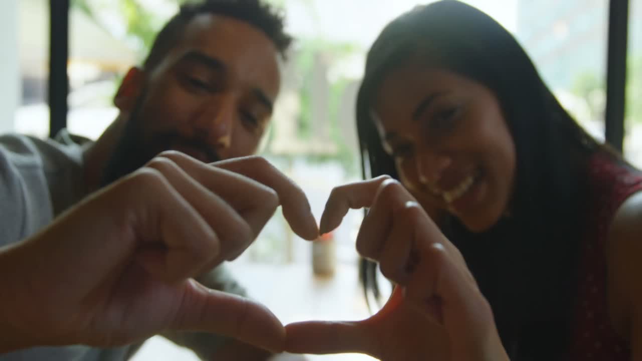Primo piano di giovane coppia multirazziale che forma un cuore con le mani in un caffè 4k