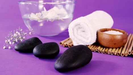 Sea-salt-in-wooden-bowl,-towel,-flowers-and-pebbles