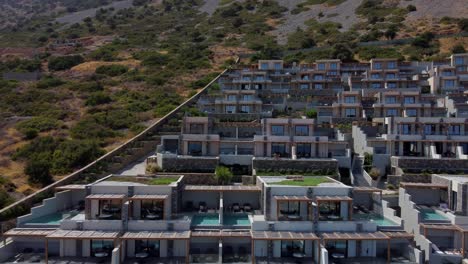 view of cayoresort in greece crete - brunette haired woman in bathing suit sitting by pool and drinking cocktail - drone flying backwards
