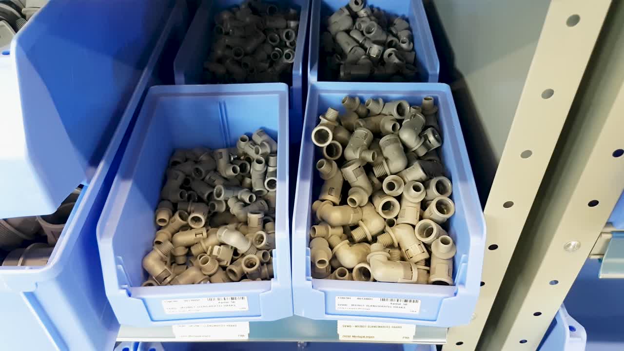 A human hand takes gray plastic connectors from a blue storage bin in an industrial metal rack on the shop floor. CLOSE UP.