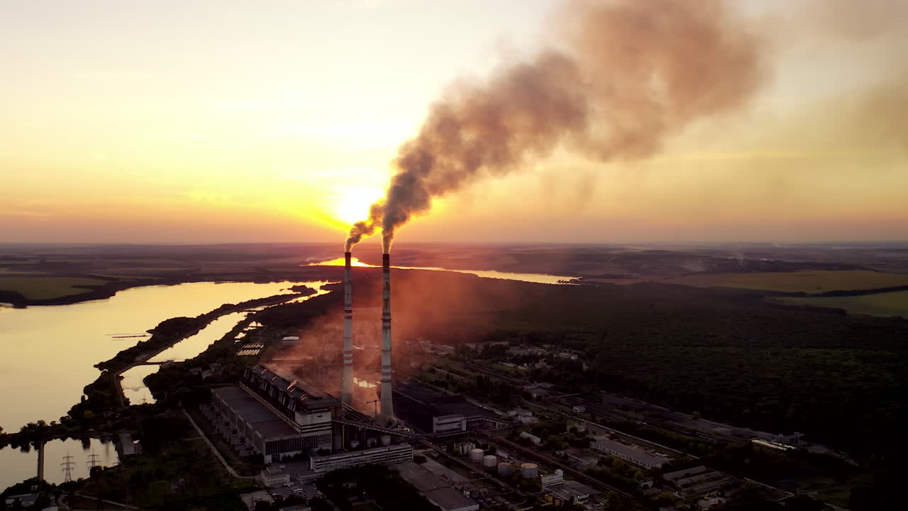 Aerial view on a huge industrial factory among nature. Dirty smoke coming into the air from factory pipes at sunset.