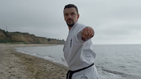 Hombre-De-Karate-Entrenando-Habilidades-De-Lucha-En-La-Playa-De-Arena-De-Cerca