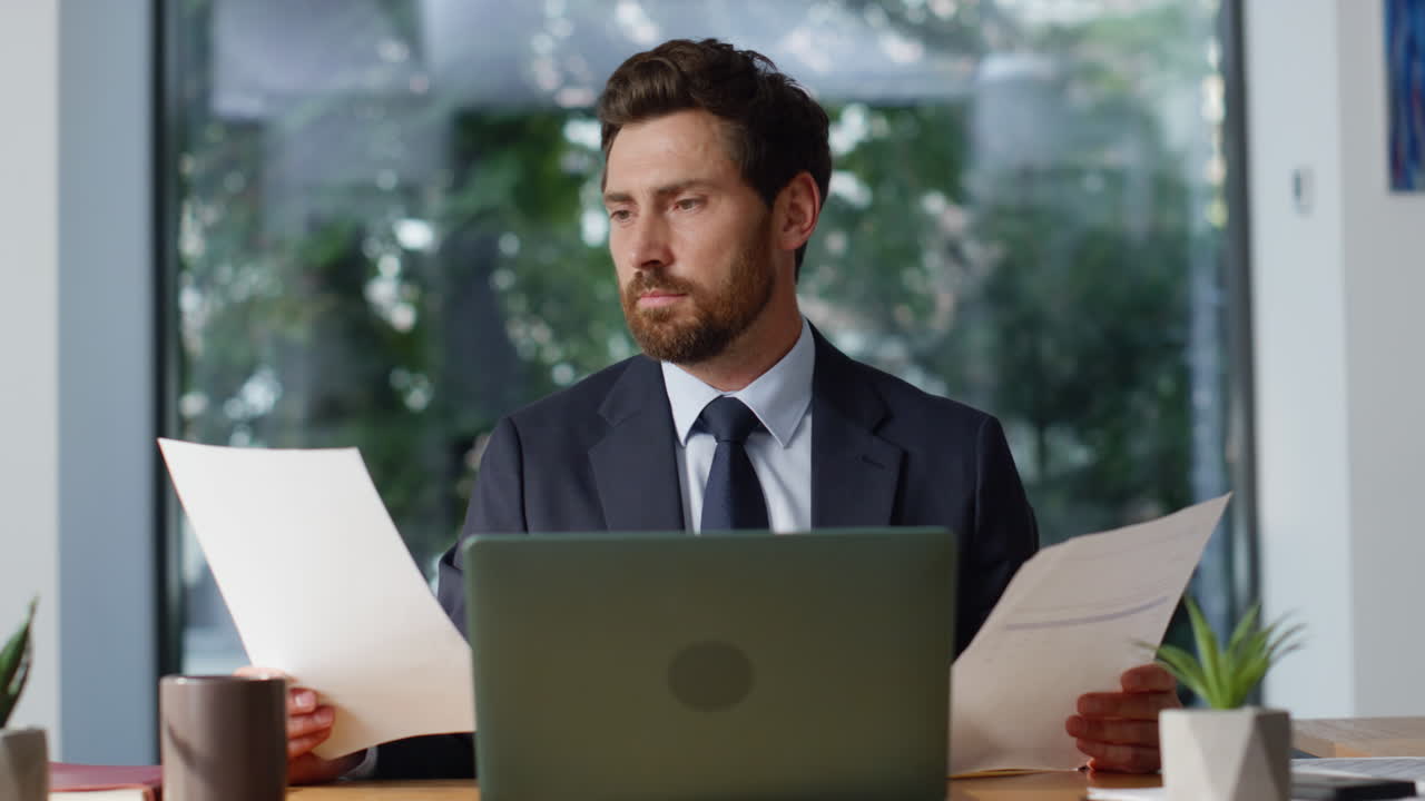 Bärtiger Unternehmer, der Dokumente prüft und sich am Arbeitsplatz zufrieden fühlt (Nahaufnahme)