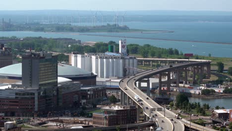 una vista aérea de la ciudad de buffalo, nueva york y su infraestructura de puentes y edificios junto al lago erie con algunas turbinas eólicas al fondo