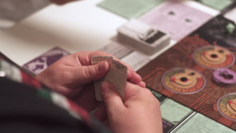 Detail-of-checking-cards-in-hand,-high-angle-of-board-game-in-background