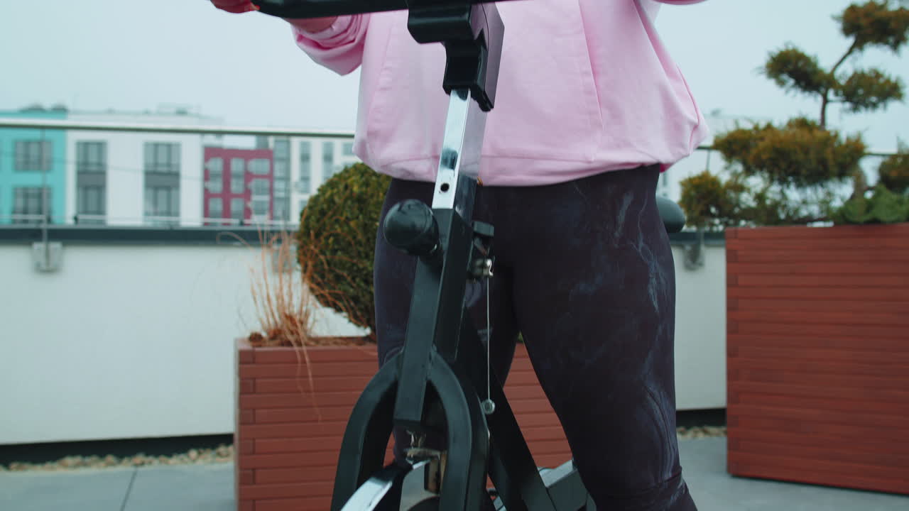 건강한 백인 여성이 집 옥상 체육관에서 정지 자전거 기계 자전거에서 운동을 하고 있습니다.