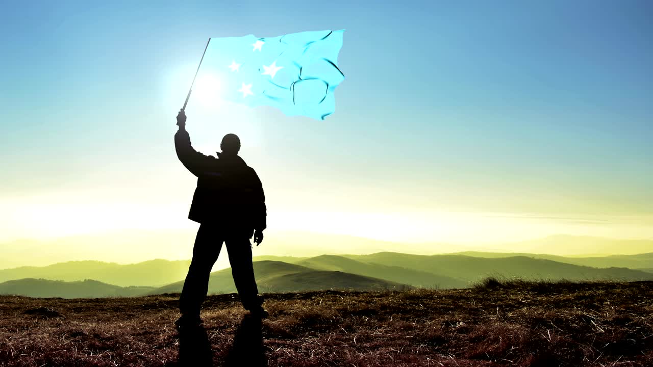 exitoso silueta hombre ganador agitando bandera de micronesia en la parte superior del pico de la montaña, fondo de bucle cinemagraph