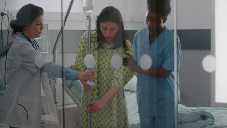medical team helping sick woman to stand up from bed holding intravenous iv fluid drip bag
