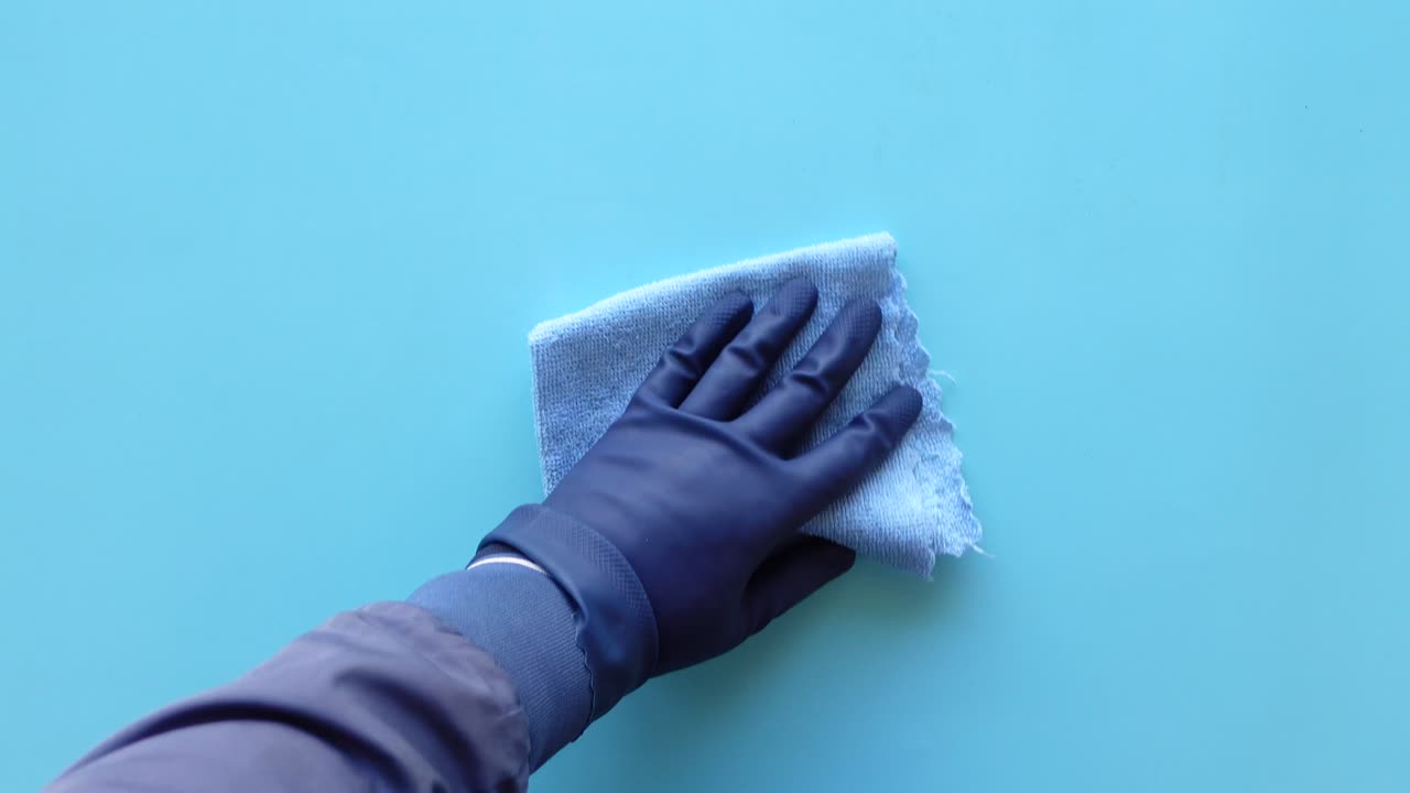 una mano con guantes limpiando una superficie azul con un paño azul
