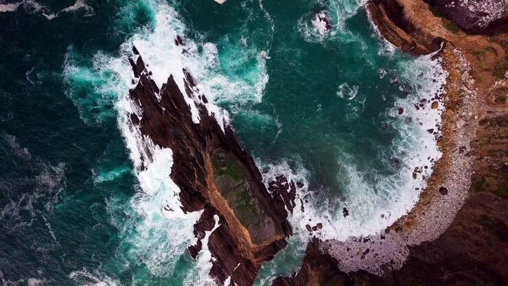 Onde turchesi dell'oceano si infrangono su una spiaggia rocciosa a Big Sur, California, ripresa ampia con drone.