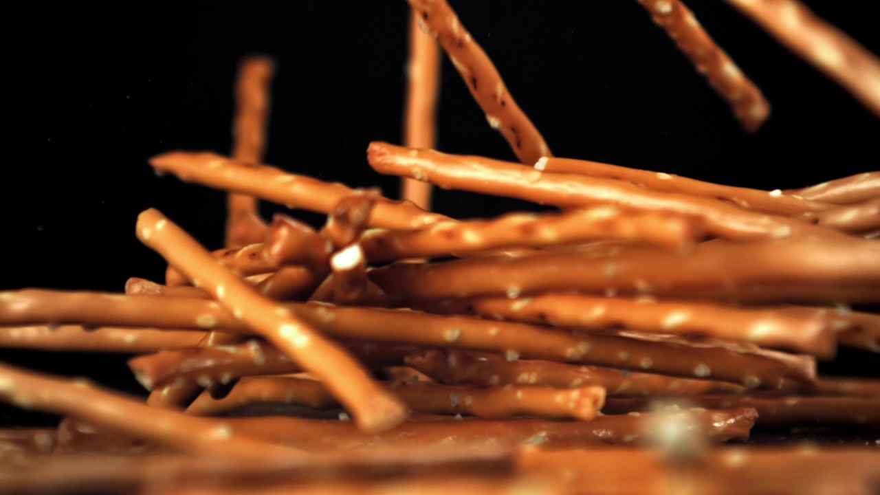 Bastoncini di pretzel salati che cadono su uno sfondo nero al rallentatore.