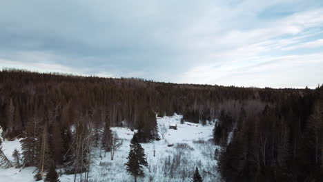 Drone-flight-over-a-small-cabin-close-to-a-frozen-river-in-winter-in-Percé,-Québec,-Canada