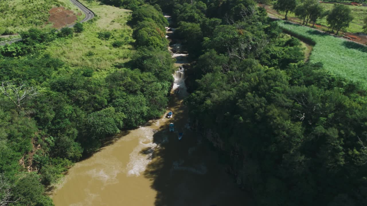 Aerial view of a river cutting through lush greenery with boats visible, flowing toward a small waterfall on the island of Mauritius. Concept of nature, adventure, river tourism, eco travel