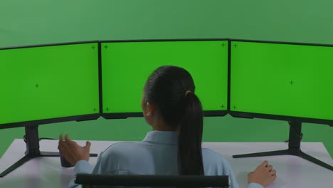 아시아 여성이 커피를 마시며 녹색 스크린 스튜디오에서 모의 다중 컴퓨터 모니터와 함께 작업하는 뒷면