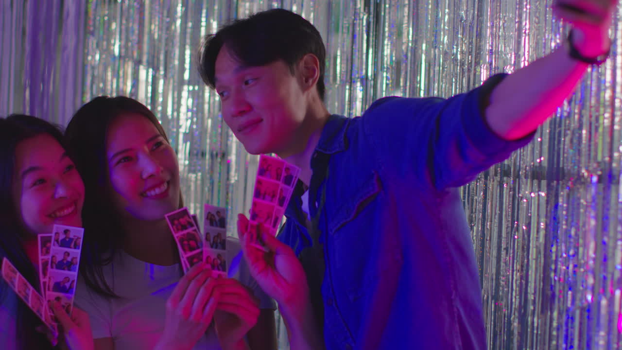 셀피를 찍는 친구 그룹이 나이트클럽이나 파니페어 4의 사진 부스에서 인쇄물을 재미있게 보고 있습니다.