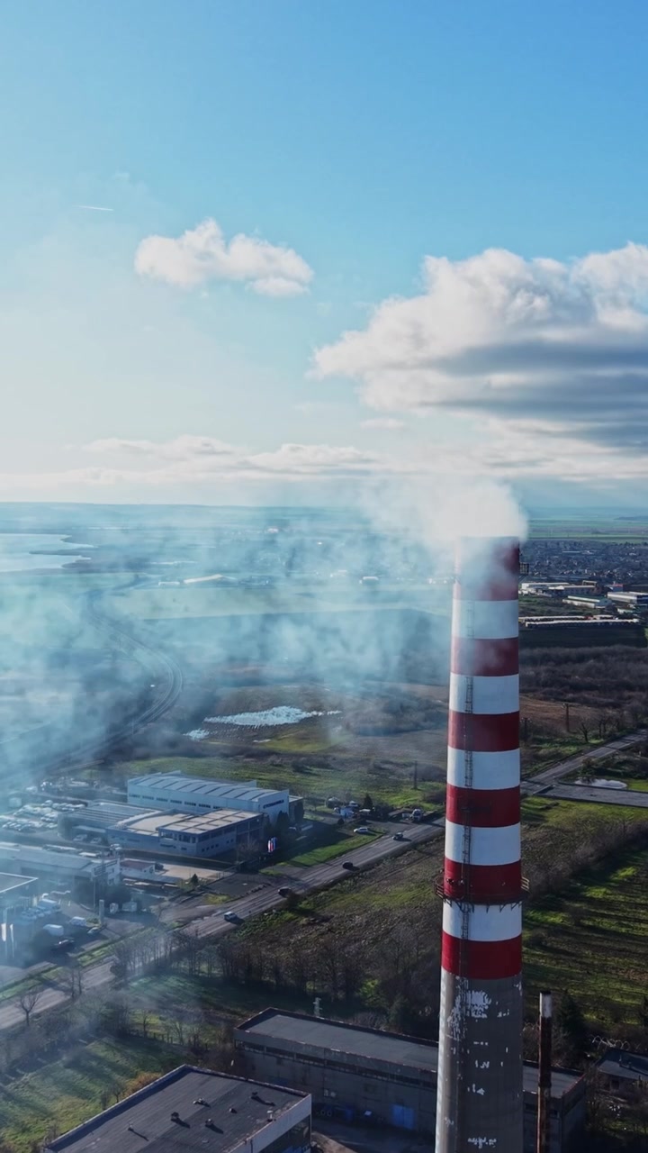 Del fumo si alza dal camino di una fabbrica vicino a uno specchio d'acqua con dei campi