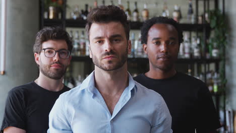 portrait of male owner of restaurant bar with team of male waiting staff standing by counter