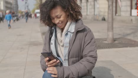 beautiful girl with afro haircut sitting on bench at city street