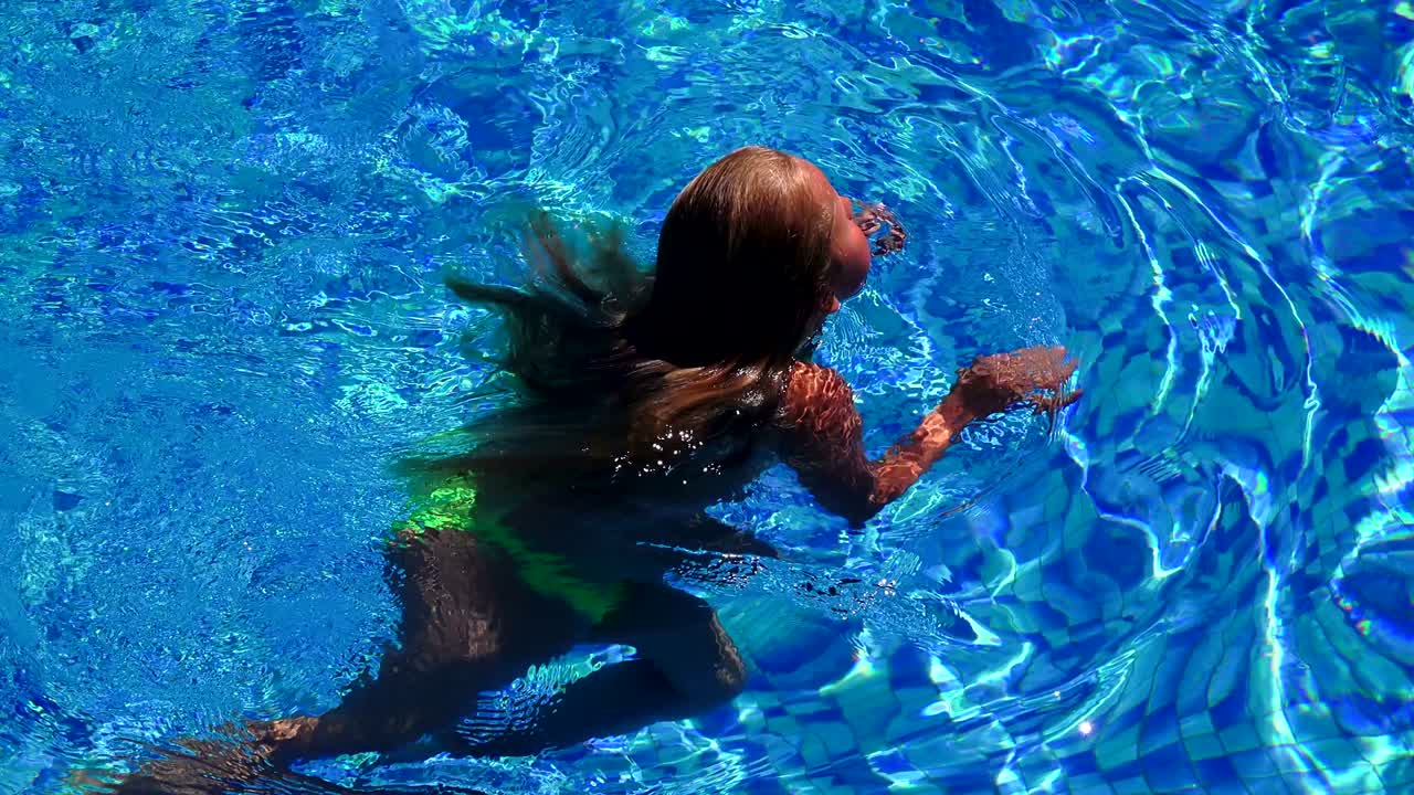 긴 금발 머리카락을 가진 예쁜 작은 소녀가 수영장에서 날아다니고, 클로즈업