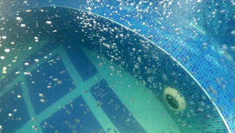 air bubbles float under the water in thermal spa pool with blue tiles