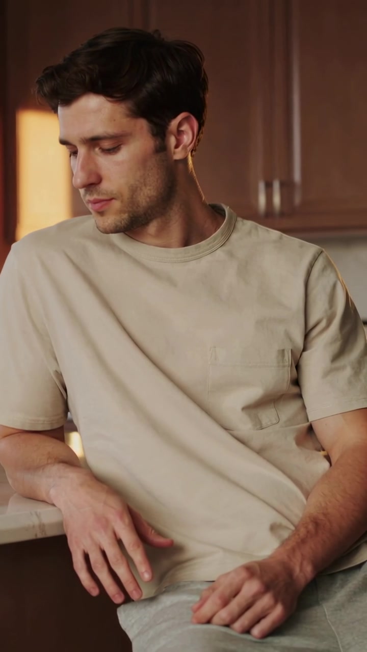 Video verticale: Uomo appoggiato con maglietta beige che abbassa la testa, mentre una lampada brilla dolcemente sul bancone della cucina.