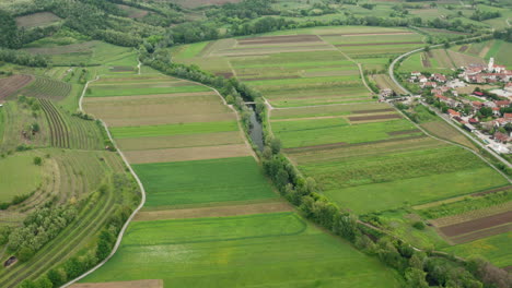 Hohe-Drohnenaufnahme-Von-Fluss--Und-Landwirtschaftsfeldern,-Straßen,-Weinbäumen-Und-Einem-Kleinen-Dorf-An-Der-Seite