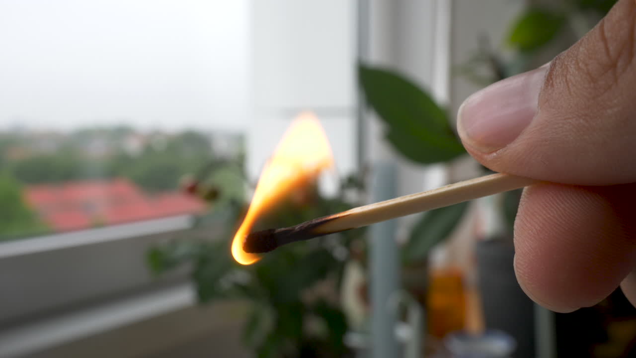 Holding a burning match stick indoors by a window.