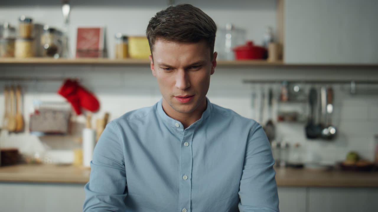 Man browsing social networks at laptop sitting in kitchen. Freelancer working.