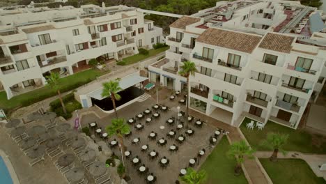 vista aérea de un complejo turístico en mallorca, españa, con un edificio de alojamiento de tres pisos con un patio frontal adornado con sillas y mesas