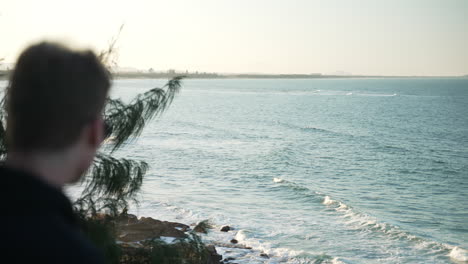 young male looking at waves in ocean from lookout on beach headland, 4k