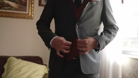 Close up of groom in green suit with floral boutonniere adjusting jacket button