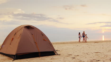 A-Woman-With-Her-Two-Daughters-Walking-Along-The-Seashore-In-The-Foreground-Is-A-Tent-For-The-Night