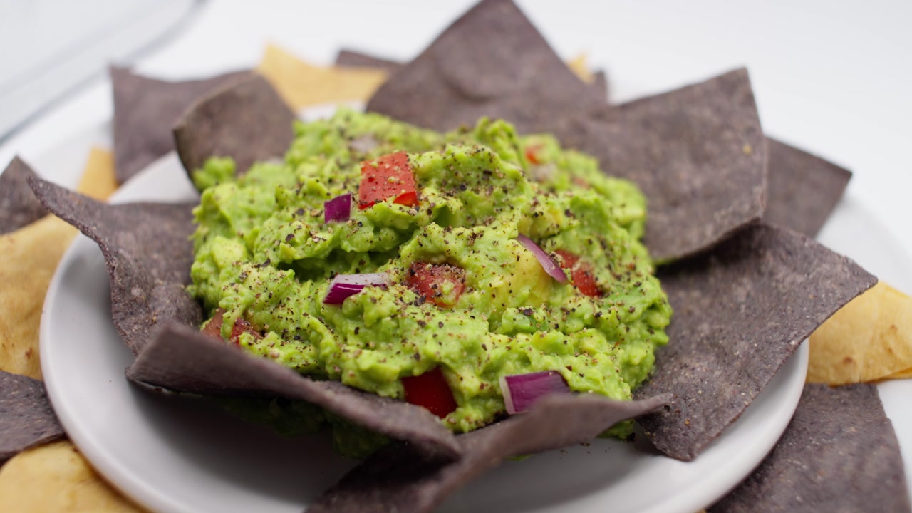 SLOW MOTION DETAIL SHOT OF A BOWL OF GUACAMOLE WITH A WITHE BACKGROUND