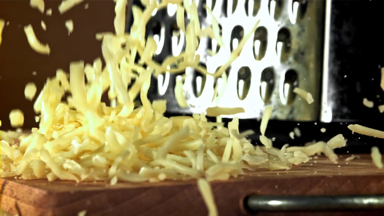 Slow Motion Grated Cheese Falling onto a Wooden Cutting Board
