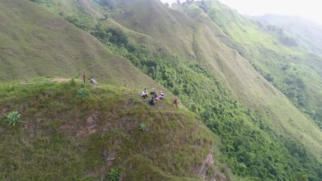 people sitting on top of hill enjoy view after climbing, drone spiral shot over green mountains