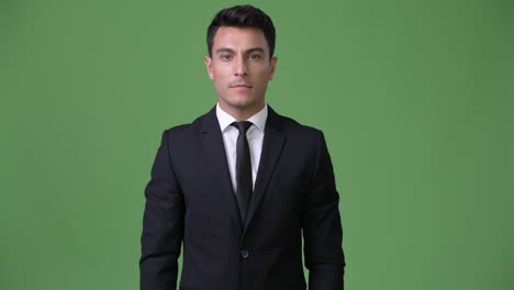 young handsome hispanic businessman against green background