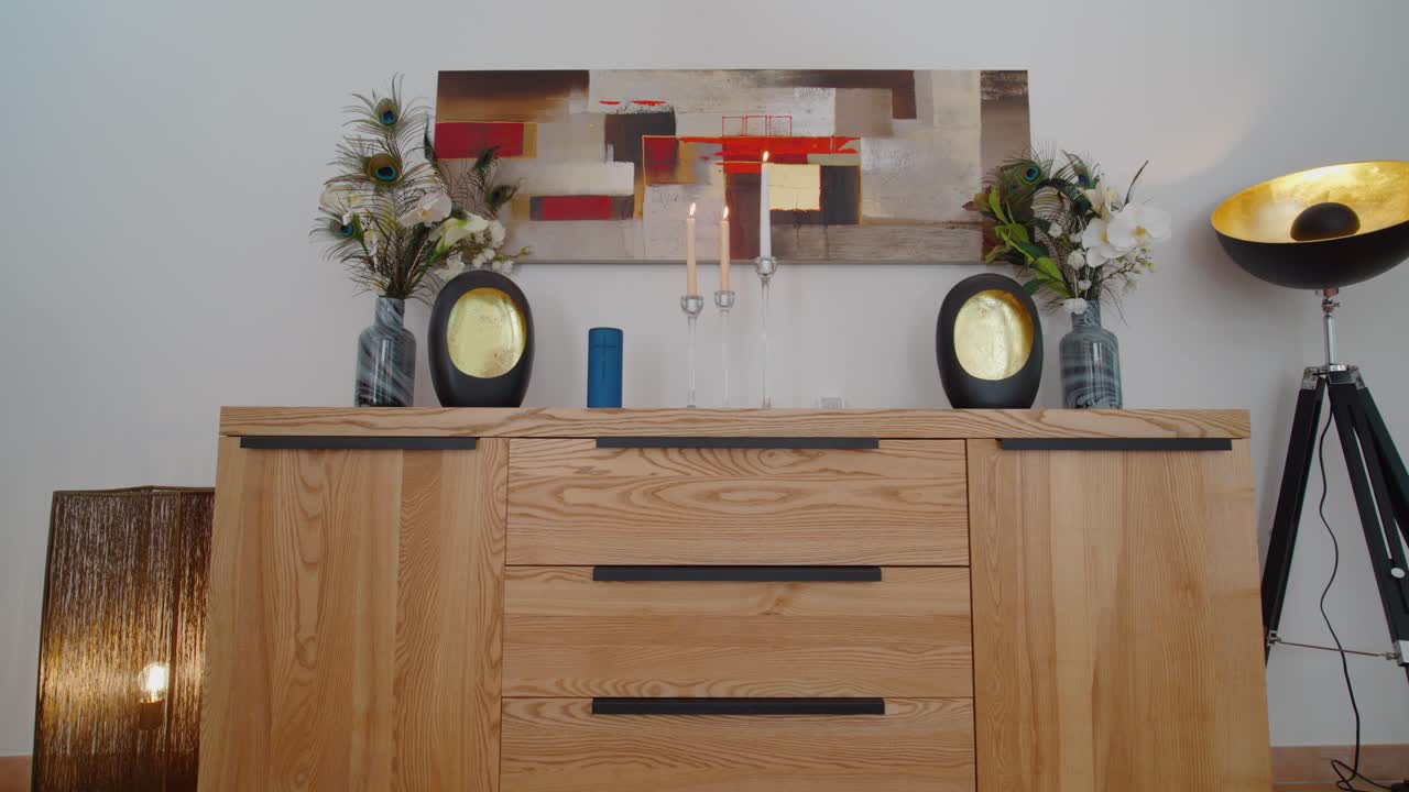 disparo lento de un gabinete de madera con velas y obras de arte colgando en la pared