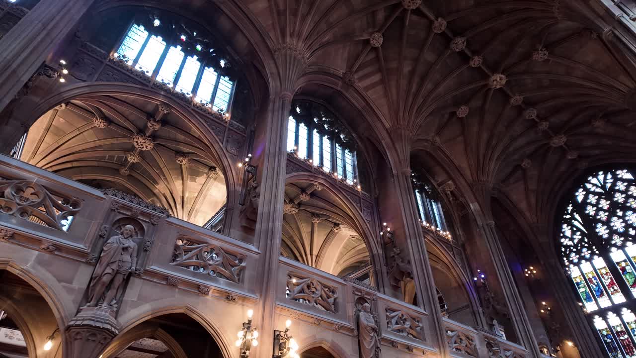 Interior view of the historic John Rylands Library in Manchester, showcasing its stunning architecture with high arches, a ribbed vault ceiling, stained glass windows, and a statue