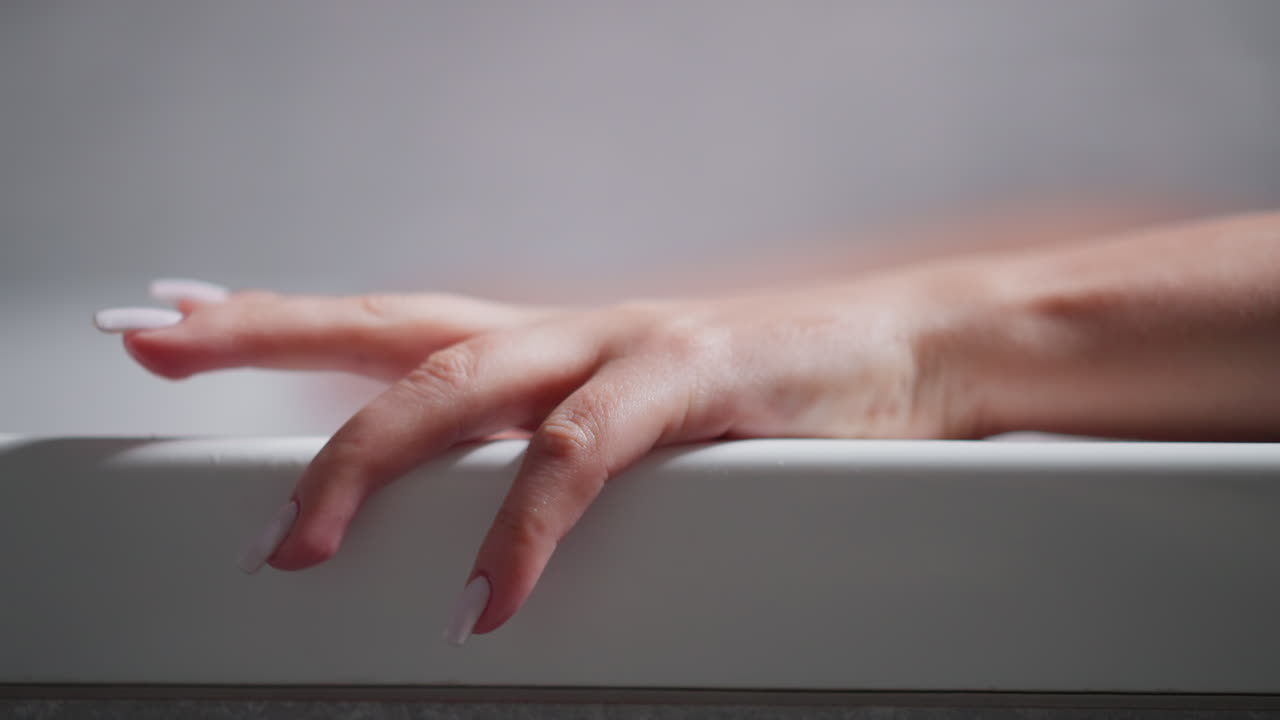 Woman taps finger on bathtub edge at home closeup. Relaxed lady enjoys taking hot bath in hotel washroom. Woman washes body and recreates in tub