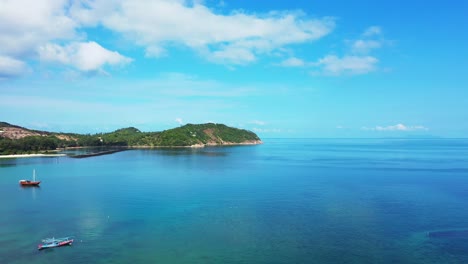 peaceful blue turquoise lagoon with fishing boats floating on calm water reflecting bright sky with white clouds in thailand