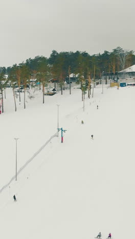 snowy mountain with wide tracks working surface lift and skiing people at snowfall against grey sky aerial view