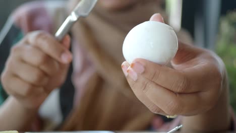 person peeling a hard-boiled egg with a knife