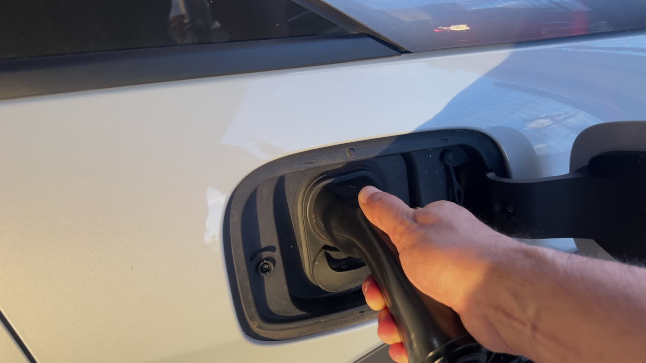 Sıcak gün batımı ışığında bir elin AC Tip 2 şarj fişini elektrikli bir arabaya bağlaması, EV şarjını ve temiz mobiliteyi gösteriyor.