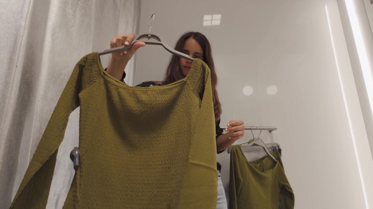 Una ragazza fa shopping di vestiti in un negozio al dettaglio, sfogliando gli scaffali e provando diversi abiti