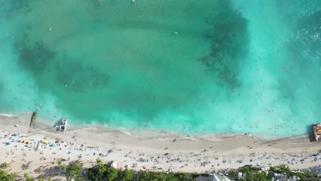 A-drone-starts-high-above-crashing-waves-and-crystal-clear-ocean-and-lowers-down-revealing-families-on-summer-vacation