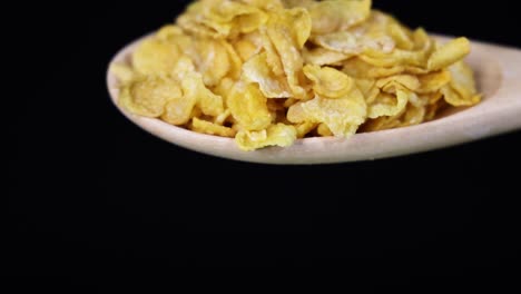 corn cereal flakes fall from a spoon in slow motion against a black backdrop, highlighting texture and movement