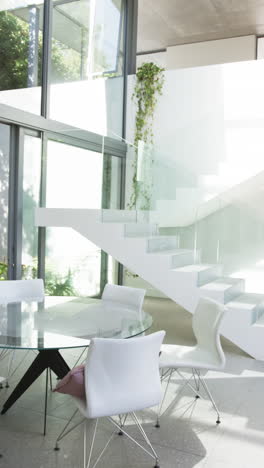 vertical video: modern dining area with glass table and white chairs in bright home
