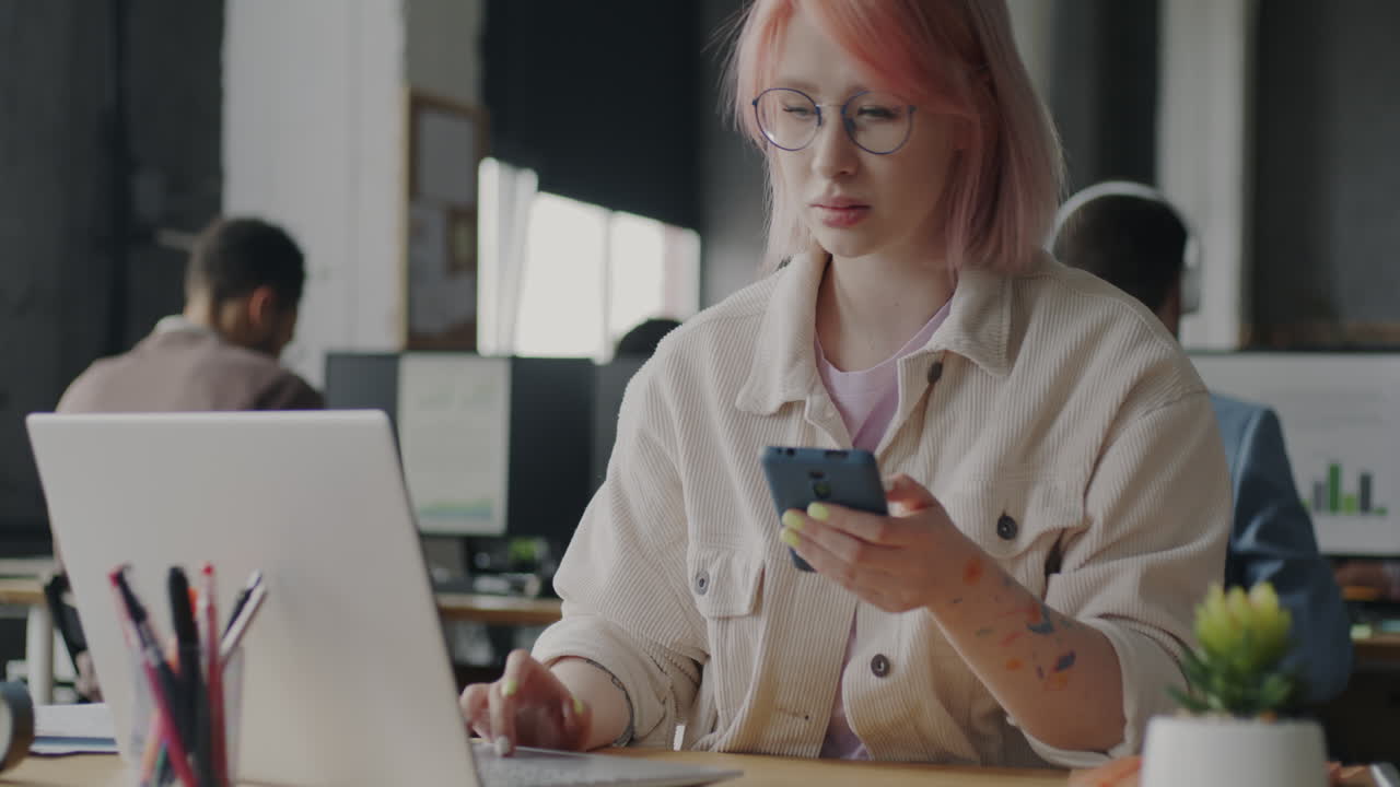 Woman in office using smartphone and laptop