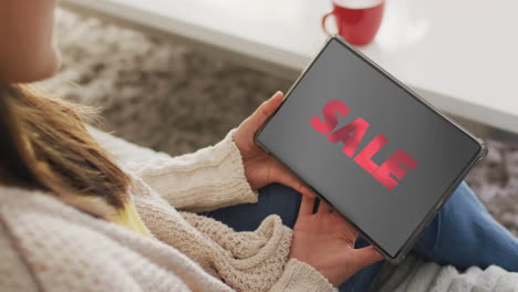 caucasian woman using tablet at home for online shopping, sale text, slow motion