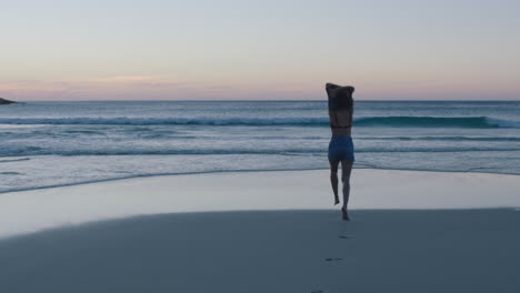 Glückliche-Junge-Frau-Am-Strand,-Die-In-Die-Wellen-Des-Ozeans-Rennt,-Tanzend,-Spielerisch-Planschend-Feiernd-Und-Im-Sommerurlaub-Spaß,-Entspannten,-Unbeschwerten-Lebensstil-Genießend